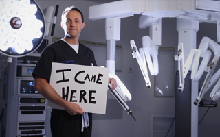 Institute for Robotic Surgery Doctor holding up sign that says I came here while in front of a surgical robot